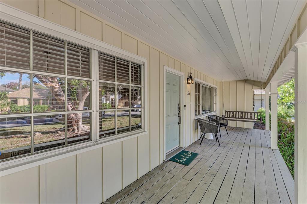 A covered wooden front porch features a light blue door, two chairs, and a hanging bench — 1726 FLOYD STREET, SARASOTA, FL