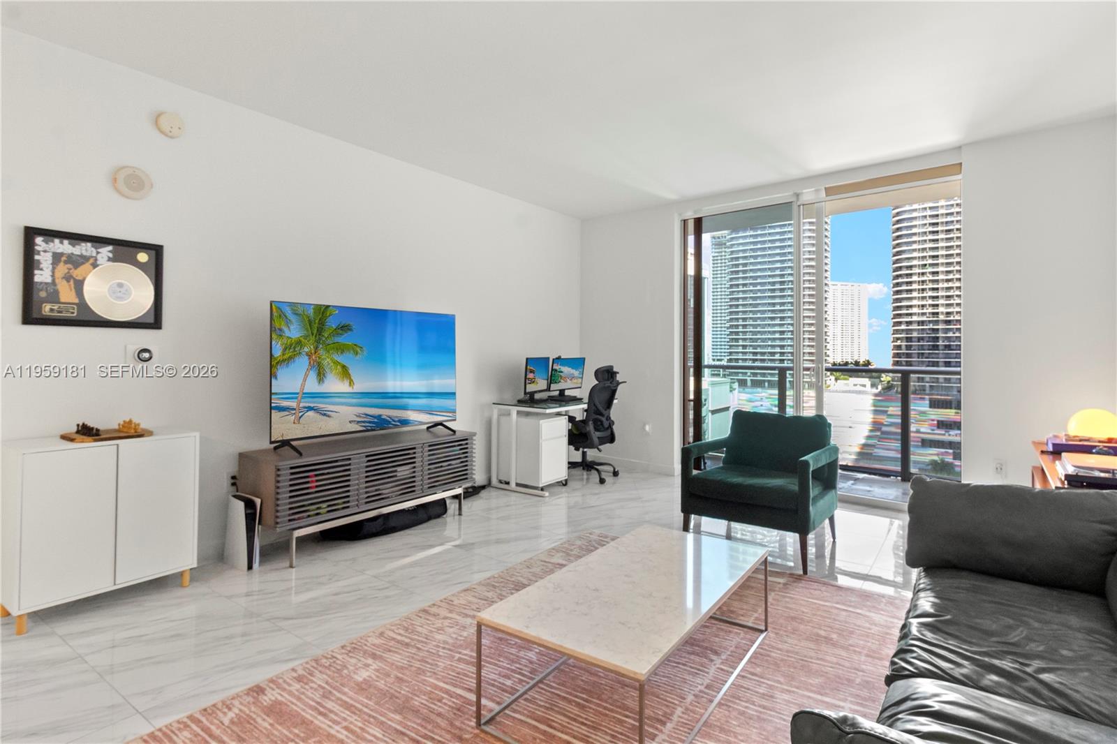 A living room features a television, desk, and balcony overlooking high-rise buildings — 1100 S Miami Ave # 1609, Miami FL 33130, MIAMI, FL