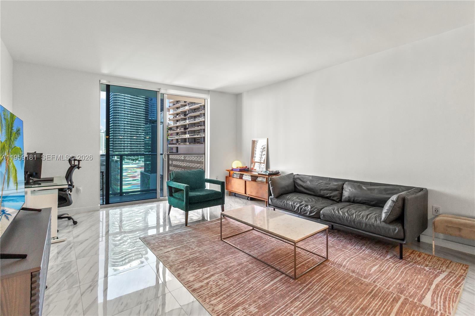 A modern living room features marble floors, a dark leather sofa, and a balcony view — 1100 S Miami Ave # 1609, Miami FL 33130, MIAMI, FL