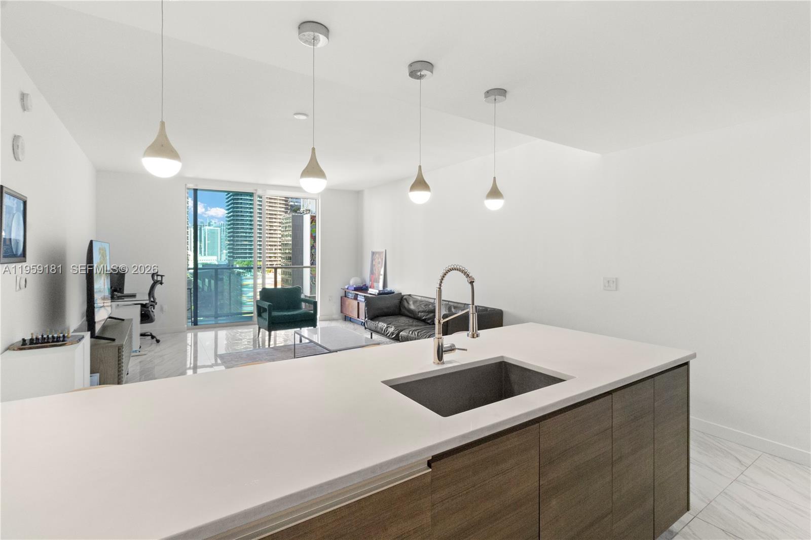 A modern kitchen island with a sink overlooks an open-concept living area with balcony access — 1100 S Miami Ave # 1609, Miami FL 33130, MIAMI, FL