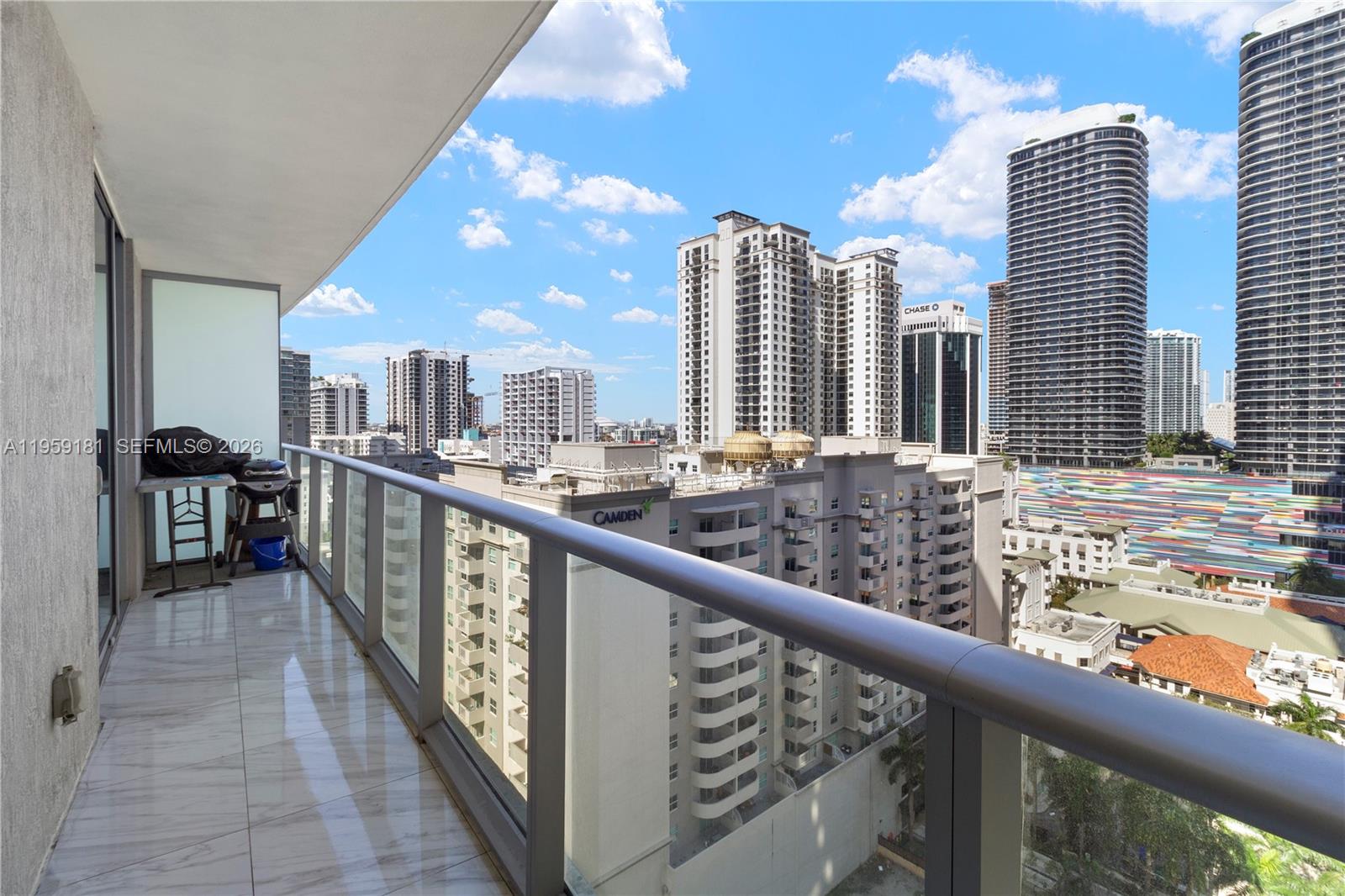 A balcony with tile flooring and a glass railing overlooks a dense urban cityscape — 1100 S Miami Ave # 1609, Miami FL 33130, MIAMI, FL