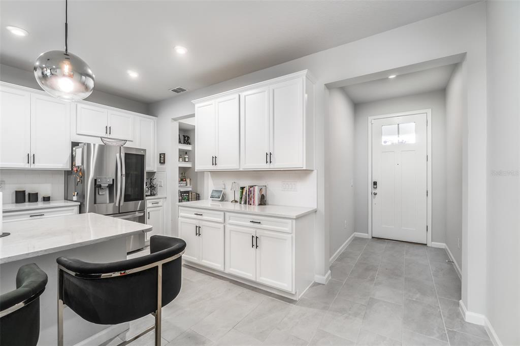 A modern kitchen features white cabinets, quartz countertops, a center island, and an entryway door — 8518 PRIMROSE WILLOW PLACE, ODESSA, FL
