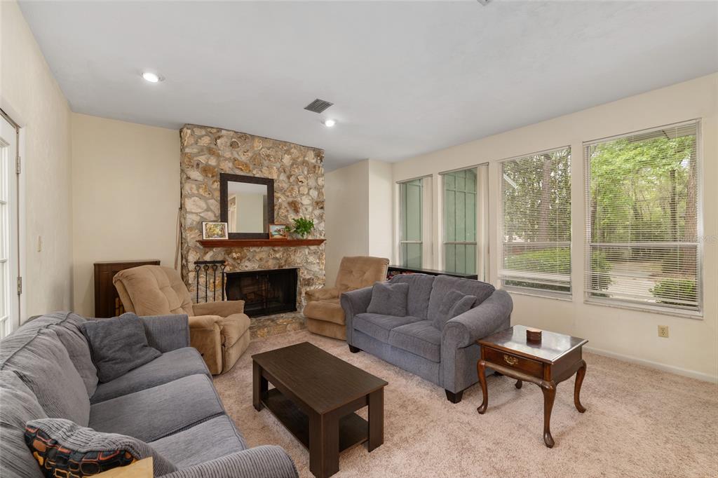 A living room features a stone fireplace, two gray sofas, and large windows with blinds — 315 NW 28TH STREET, GAINESVILLE, FL
