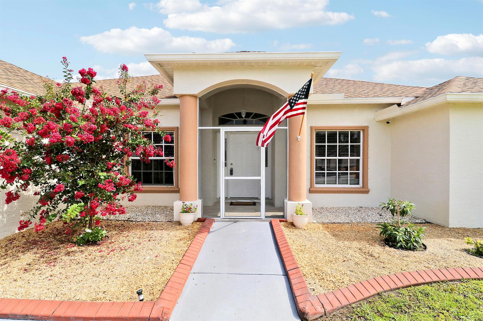 The exterior of a single-story house features a front walkway, a screened entryway, and landscaping — 611 SW Saragossa Avenue, FL 34953, FL