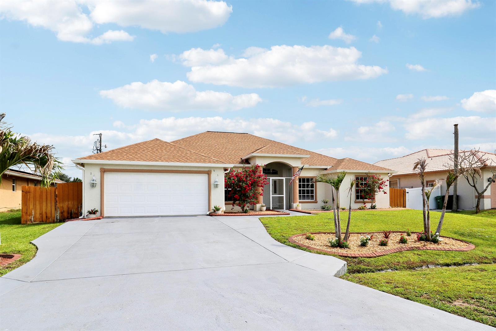 A single-story suburban house with a two-car garage, tan stucco exterior, and a landscaped yard — 611 SW Saragossa Avenue, FL 34953, FL