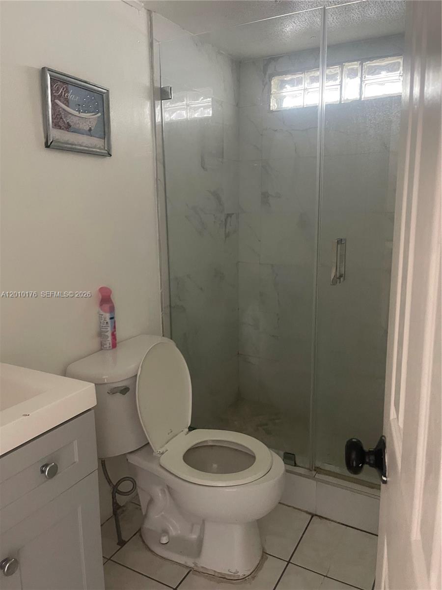 A bathroom features a gray vanity, a white toilet, and a glass-enclosed walk-in shower — 12401 W Okeechobee Rd, Hialeah FL 33018, HIALEAH, FL