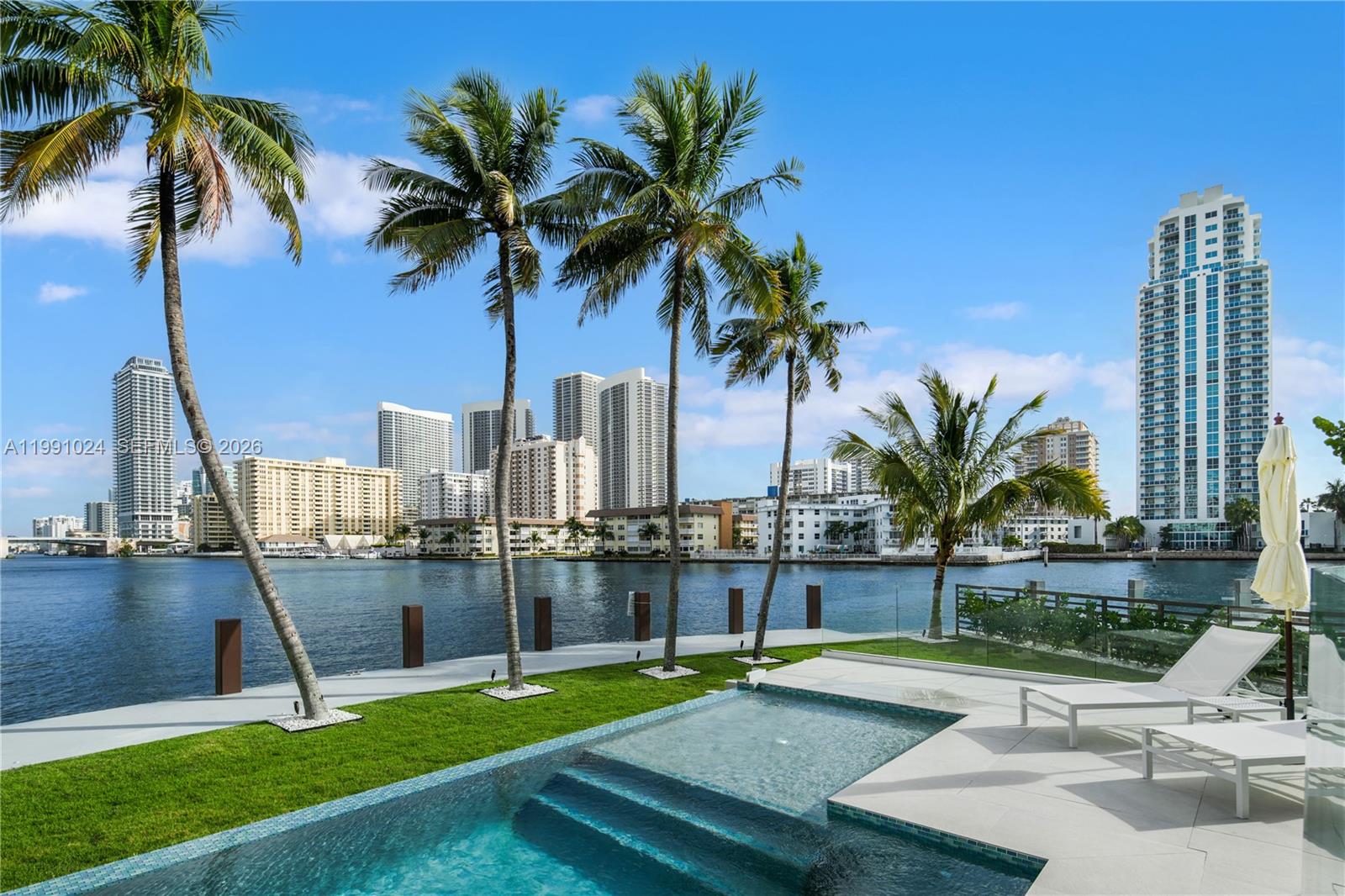 A swimming pool sits on a patio overlooking a bay with city buildings in the background — 501 Palm Dr, Hallandale Beach FL 33009, HALLANDALE BEACH, FL