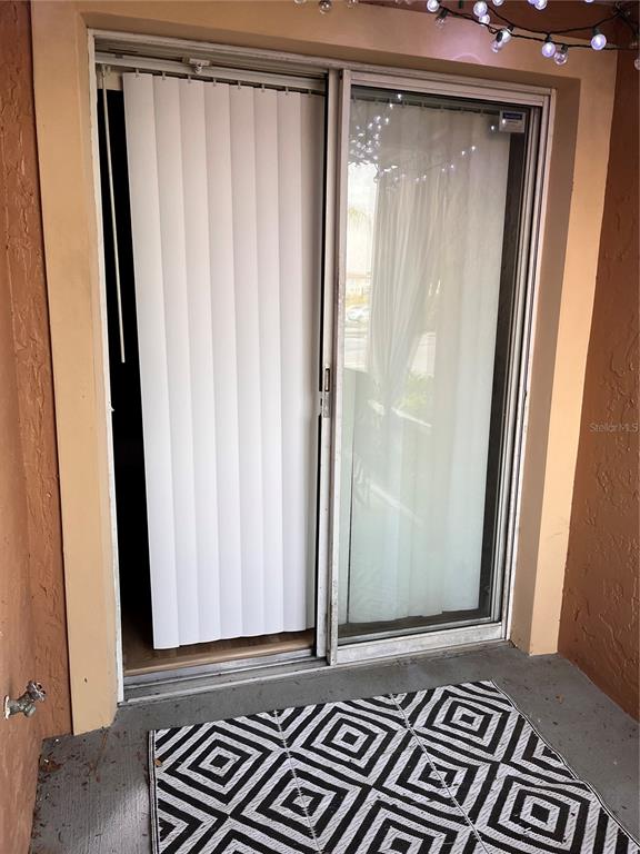 A sliding glass door with vertical blinds opens onto a patio with a patterned rug — 8304 WATERVIEW WAY UNIT 8304, WINTER HAVEN, FL