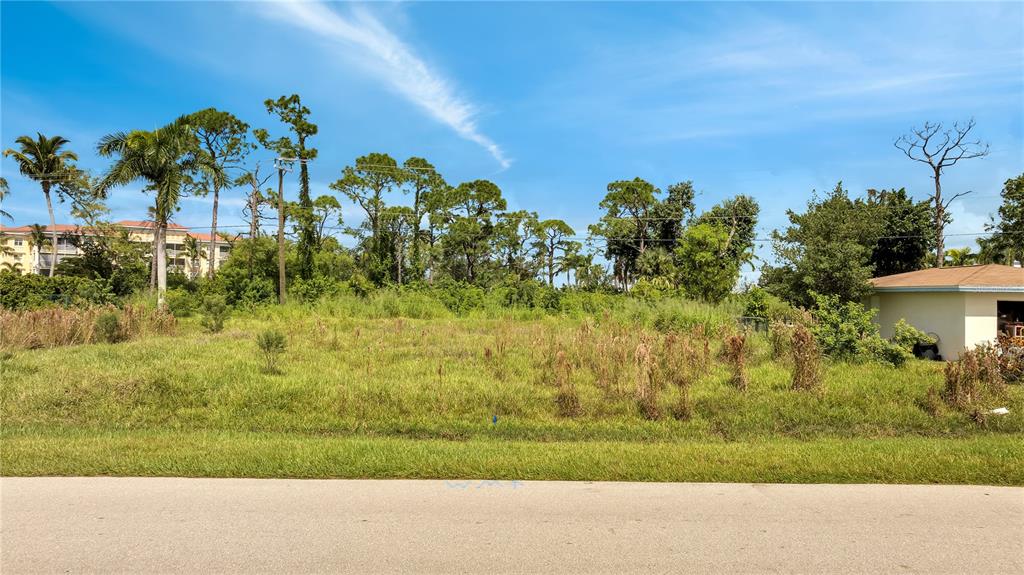 A vacant, grassy lot with scattered vegetation sits next to a house under a blue sky — 230 POMPANO TERRACE, PUNTA GORDA, FL