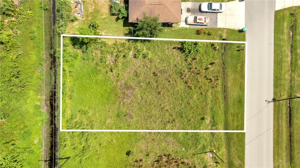An aerial view shows a rectangular, grass-covered vacant lot bordered by a road and vegetation — 230 POMPANO TERRACE, PUNTA GORDA, FL