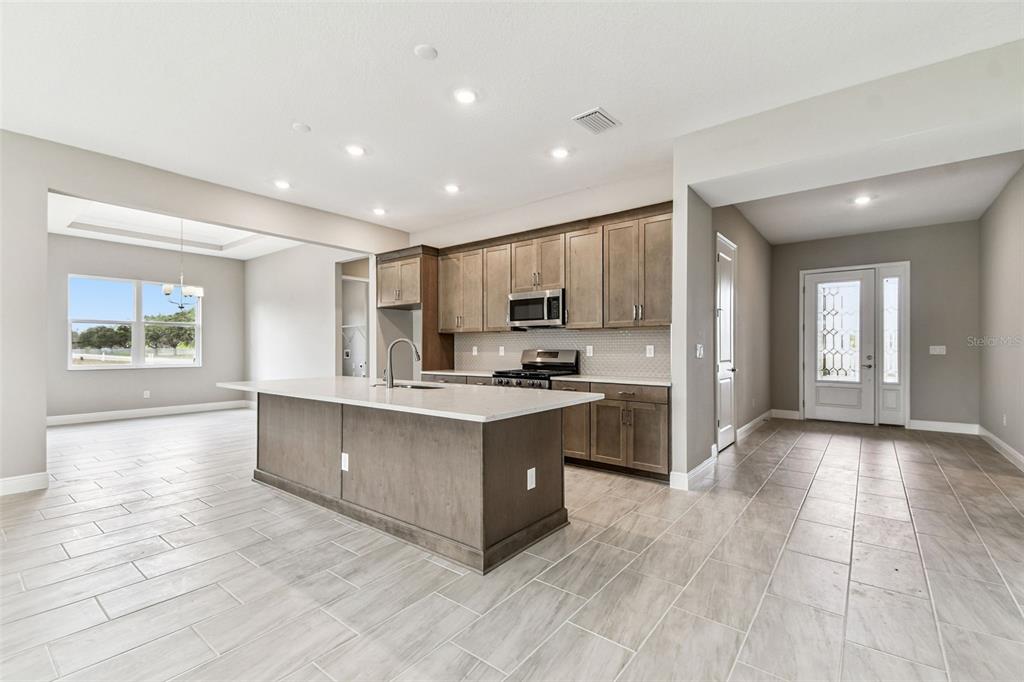 A modern kitchen features a large island, wood cabinets, and light tile flooring — 12305 WHITE BLOSSOM COURT, PARRISH, FL