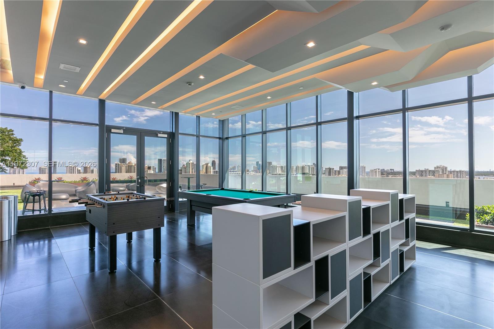A game room with a foosball table, pool table, and shelving unit overlooks a city skyline — 19790 W Dixie Hwy 1004 Hwy, FL 33180, FL