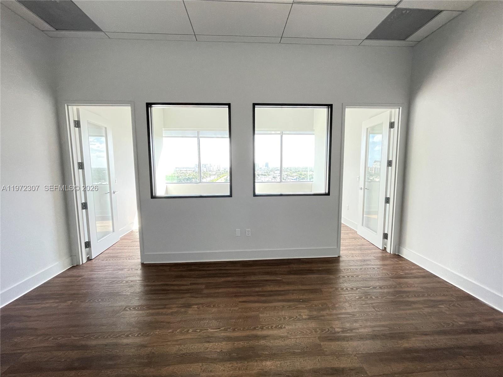An office space features wood-look flooring, two glass-paned doors, and two windows overlooking a city — 19790 W Dixie Hwy 1004 Hwy, FL 33180, FL