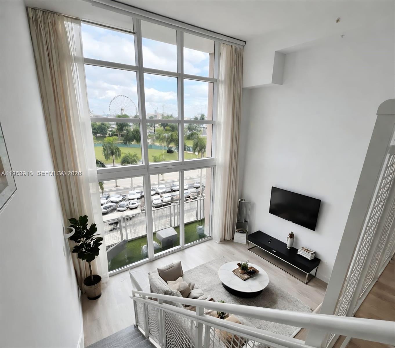 A living room features a gray sofa, a staircase with metal railings, and floor-to-ceiling windows — 253 NE 2nd St # 433, Miami FL 33132, MIAMI, FL