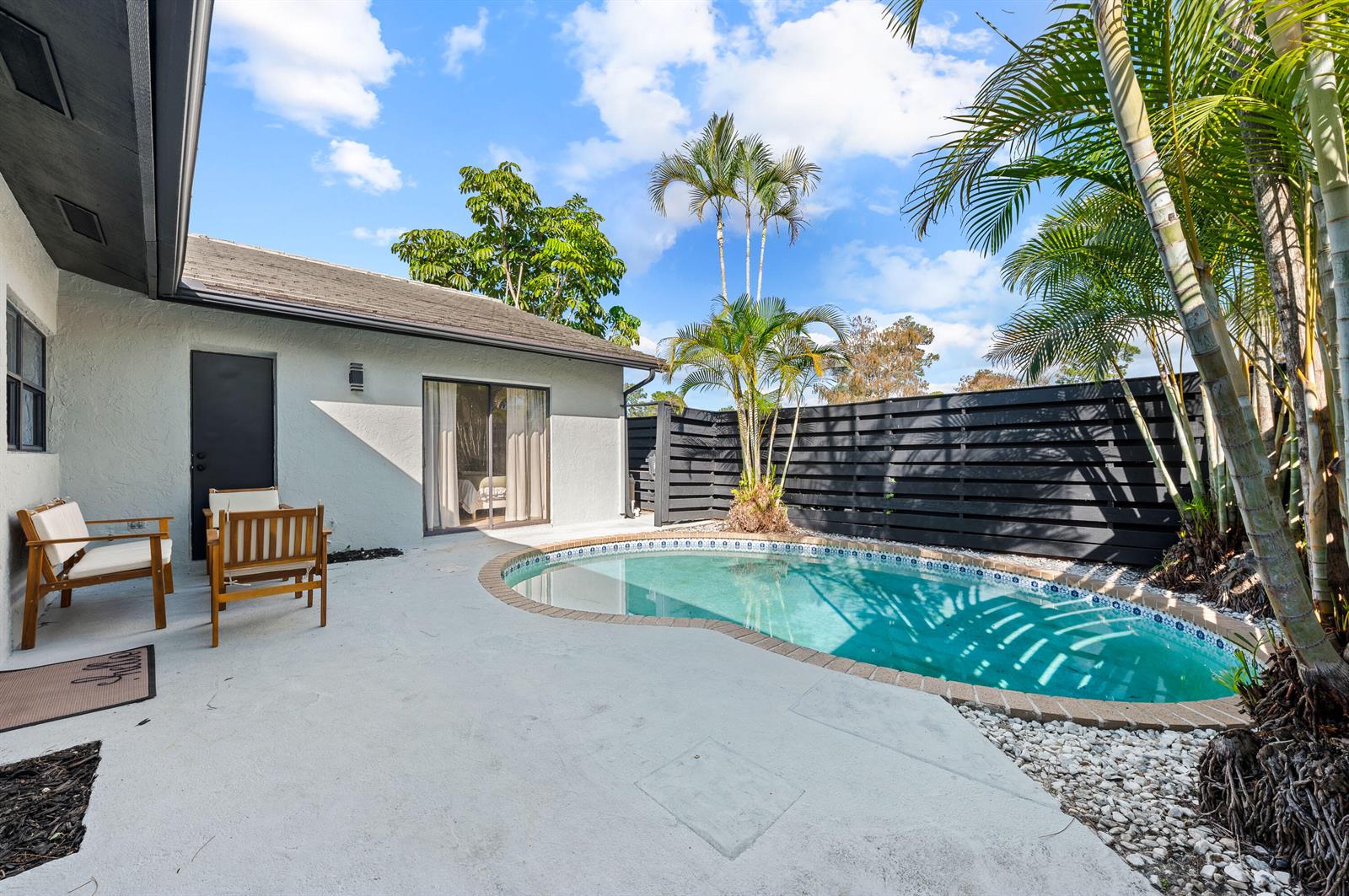 A backyard patio features a small kidney-shaped pool, wooden chairs, and a black privacy fence — 1277 Periwinkle Place, Wellington FL 33414, WELLINGTON, FL