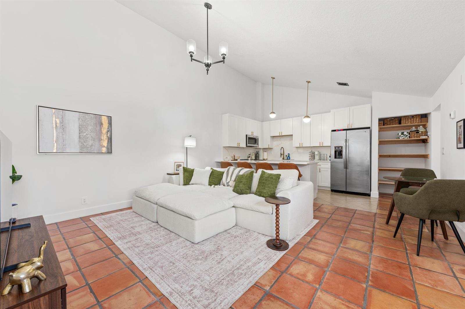 A living room and kitchen open-concept space features white cabinetry, terracotta tile floors, and furniture — 1277 Periwinkle Place, Wellington FL 33414, WELLINGTON, FL