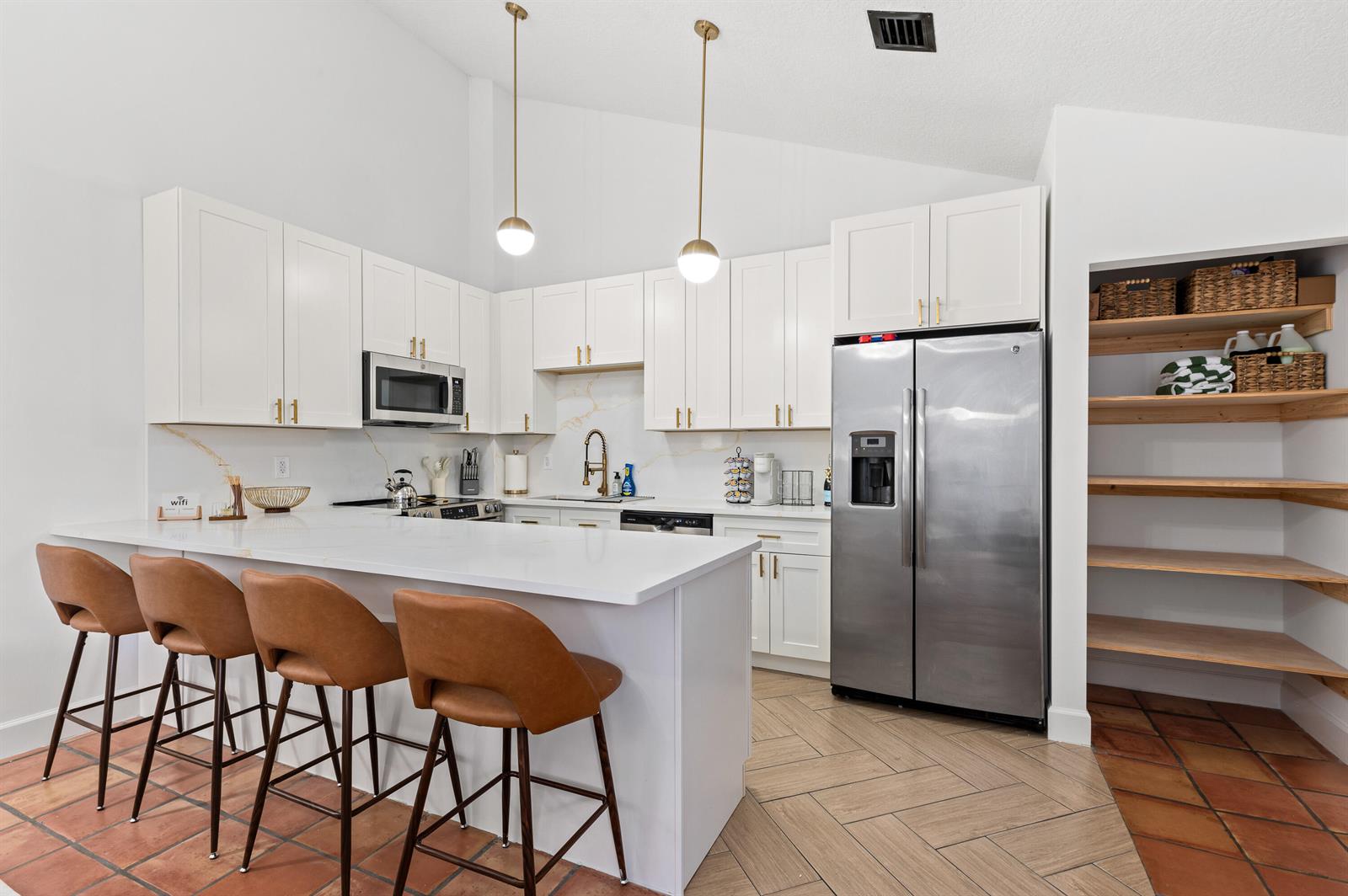 A modern kitchen features white cabinets, stainless steel appliances, a breakfast bar, and tiled flooring — 1277 Periwinkle Place, Wellington FL 33414, WELLINGTON, FL
