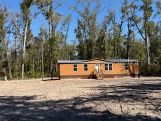 A single-story tan manufactured home sits on a cleared dirt lot surrounded by trees — 1668 NE 592ND STREET, OLD TOWN, FL