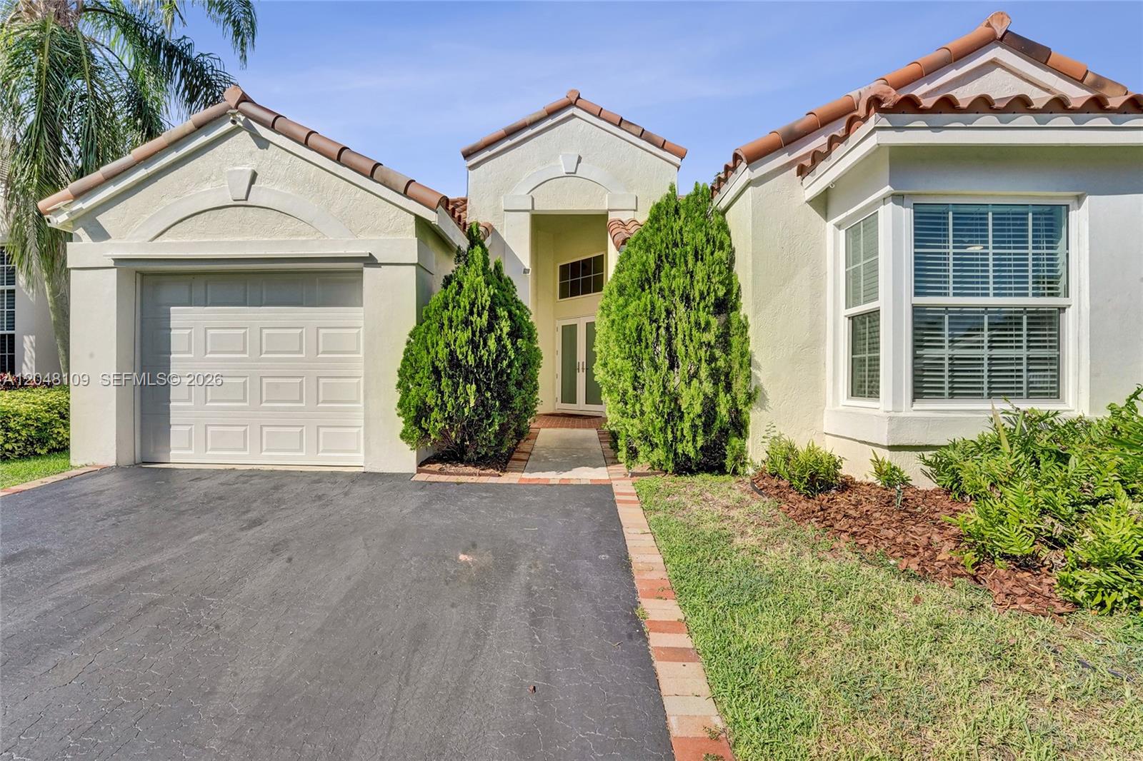The exterior of a single-story house features a garage, a front entrance, and landscaping — 507 Bridgeton Rd, Weston FL 33326, WESTON, FL
