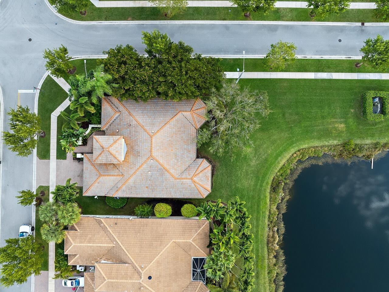 An aerial view shows two houses with tiled roofs situated near a pond and street — 9724 Via Grandezza W, Wellington FL 33411, WELLINGTON, FL