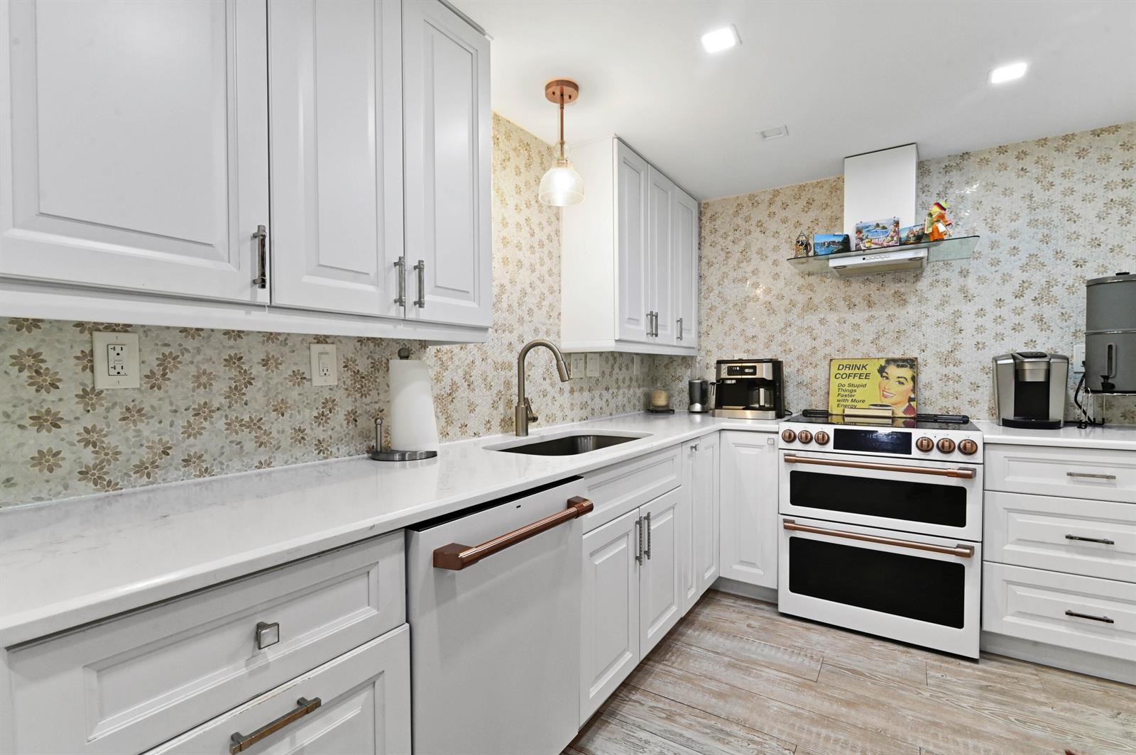 A kitchen features white cabinets, copper hardware, a floral backsplash, and a double oven range — 2840 S Ocean Boulevard # 109, Palm Beach FL 33480, PALM BEACH, FL