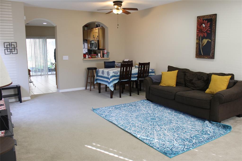 A living room with beige carpet, a brown sofa, and a dining area with a pass-through — 5815 FISHHAWK RIDGE DRIVE, LITHIA, FL