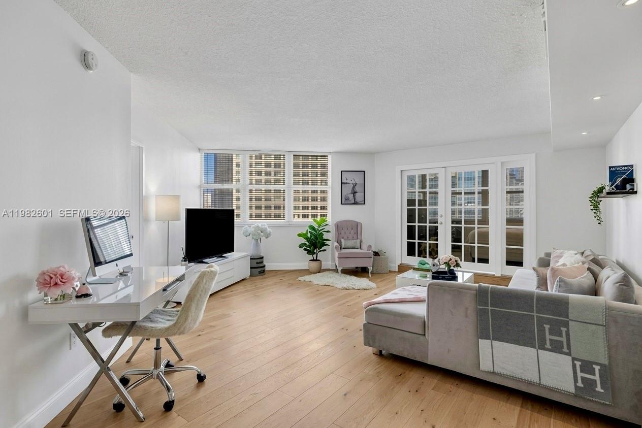 A bright living room features light wood flooring, a desk, a sofa, and glass doors — 801 Brickell Bay Dr # 1262, Miami FL 33131, MIAMI, FL