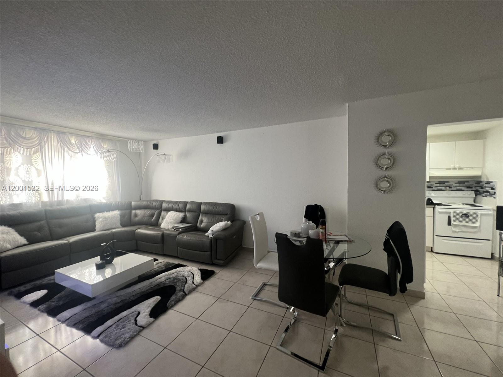 A living room features a grey sectional sofa, a glass dining table, and tile flooring — 666 W 81st St # 407, Hialeah FL 33014, HIALEAH, FL