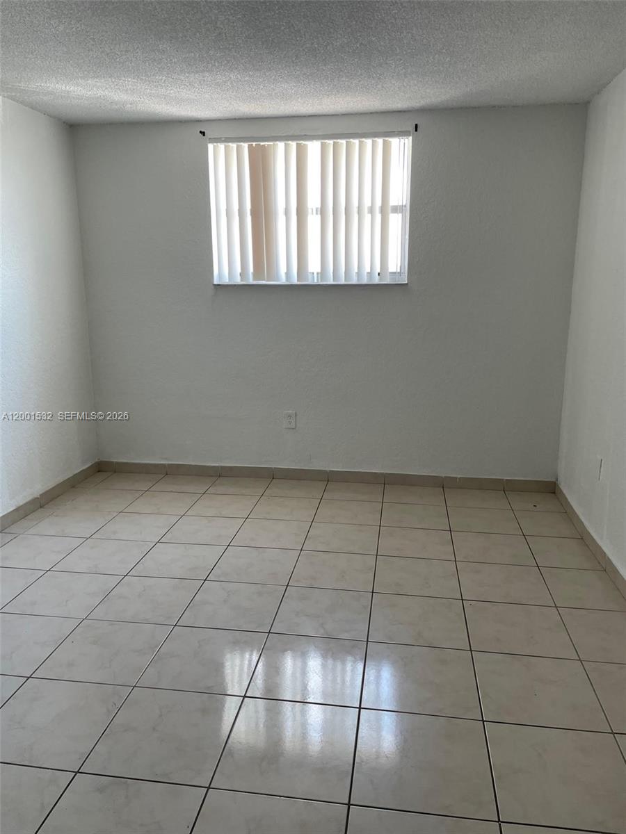 An empty room features white walls, a single window with vertical blinds, and tiled flooring — 666 W 81st St # 407, Hialeah FL 33014, HIALEAH, FL
