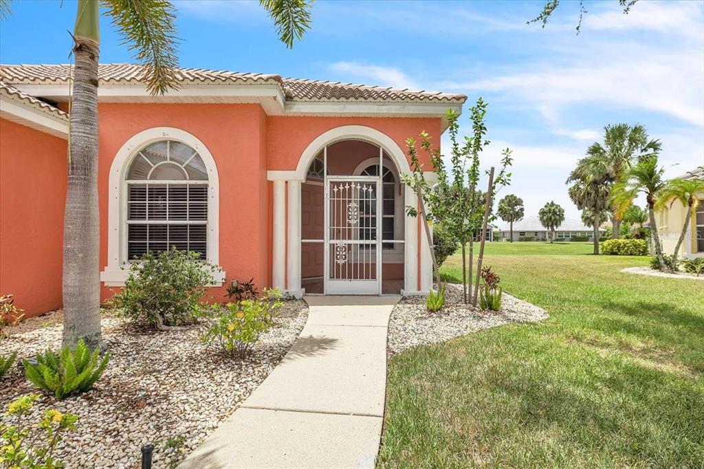 A peach-colored house exterior features an arched entryway with a white screen door and walkway — 10316 ARROWHEAD DRIVE, PUNTA GORDA, FL