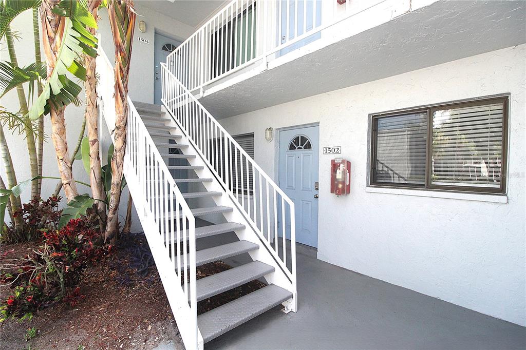 An exterior view shows a ground-level apartment entrance and a staircase leading to unit 1504 — 5310 26TH STREET W UNIT 1502, BRADENTON, FL