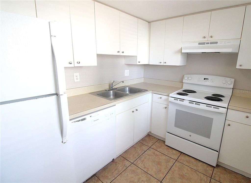 A kitchen features white cabinets, white appliances, a double sink, and tiled flooring — 5310 26TH STREET W UNIT 1502, BRADENTON, FL