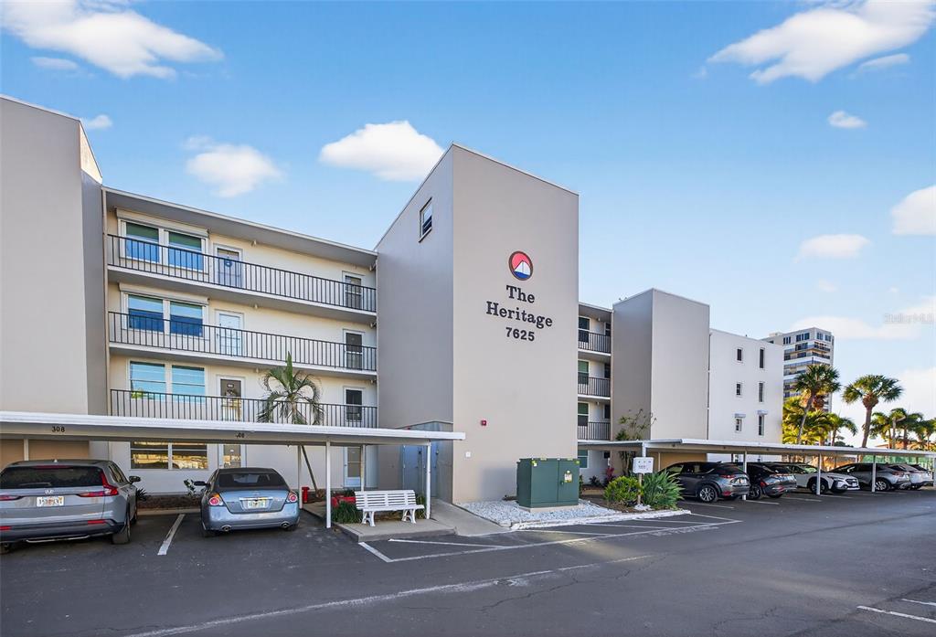 The exterior of a multi-story apartment building with covered parking and a paved lot — 7625 SUN ISLAND DRIVE S UNIT 207, SOUTH PASADENA, FL