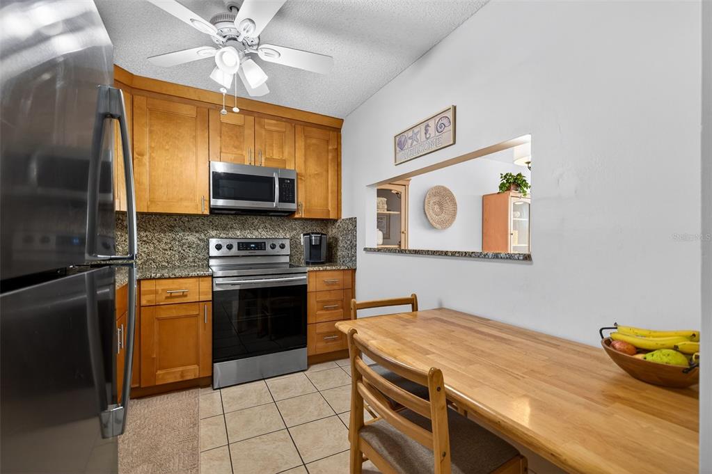 A kitchen with wood cabinets, granite countertops, stainless steel appliances, and an attached dining table — 7625 SUN ISLAND DRIVE S UNIT 207, SOUTH PASADENA, FL