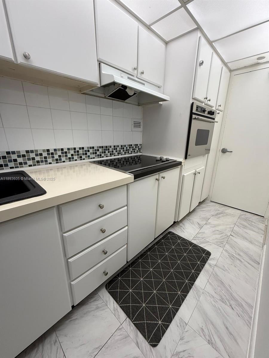 A galley kitchen features white cabinets, a black cooktop, a wall oven, and tiled flooring — 1000 West Ave # 306, Miami Beach FL 33139, MIAMI BEACH, FL