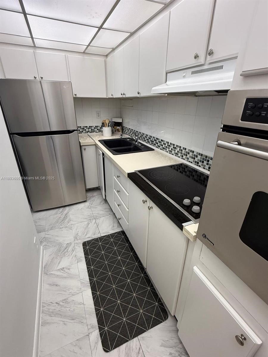 A galley kitchen features white cabinets, stainless steel appliances, and a black tiled backsplash — 1000 West Ave # 306, Miami Beach FL 33139, MIAMI BEACH, FL