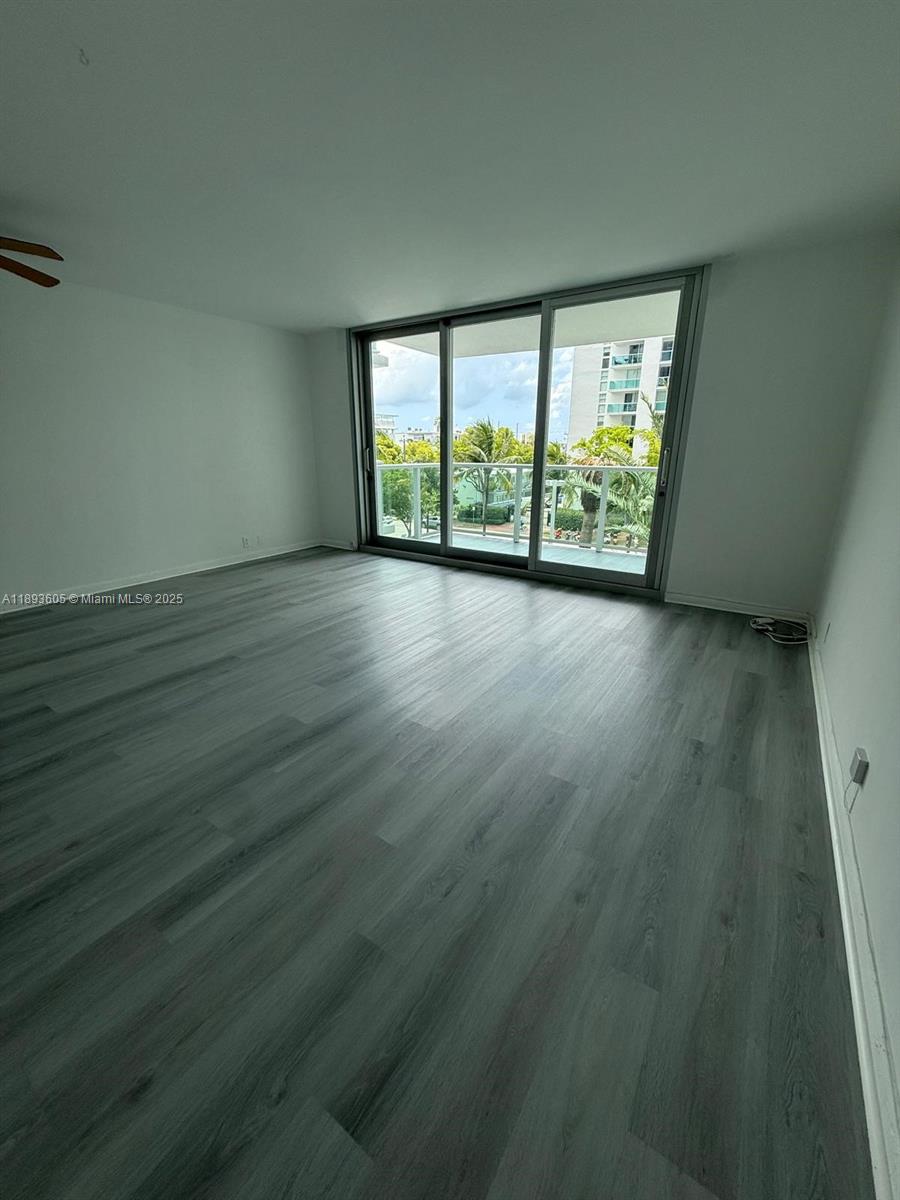 An empty room features gray wood-look flooring and a large sliding glass door to a balcony — 1000 West Ave # 306, Miami Beach FL 33139, MIAMI BEACH, FL