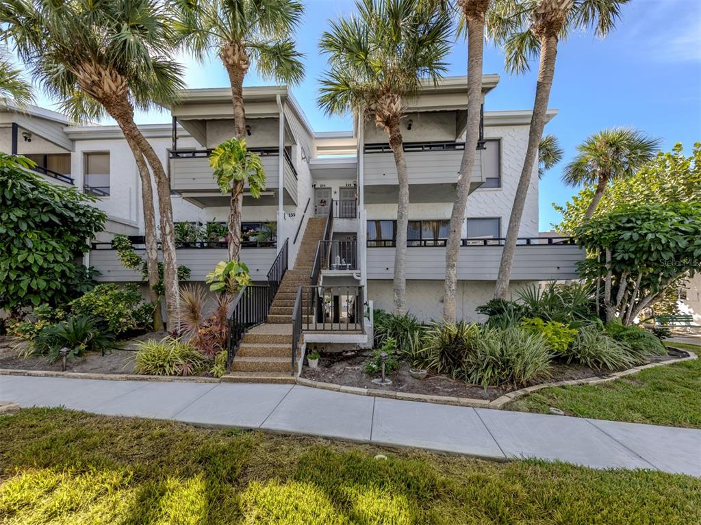 A two-story apartment building features a central staircase leading to upper-level balconies and palm trees — 1555 TARPON CENTER DRIVE UNIT 255, VENICE, FL