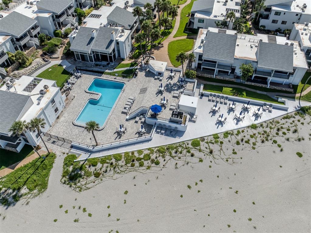 An aerial view shows a swimming pool and patio area situated next to a sandy beach — 1555 TARPON CENTER DRIVE UNIT 255, VENICE, FL