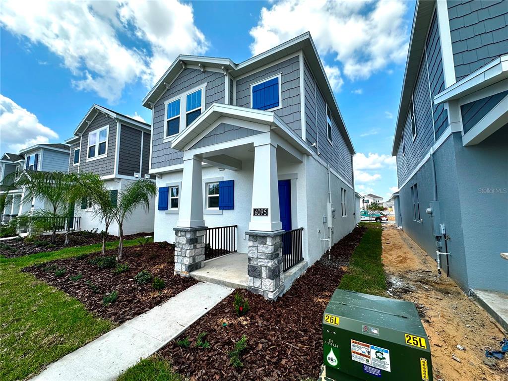 A two-story house with gray siding, stone-based porch columns, and blue shutters under a blue sky — 6095 WELLBEING WAY, CLERMONT, FL