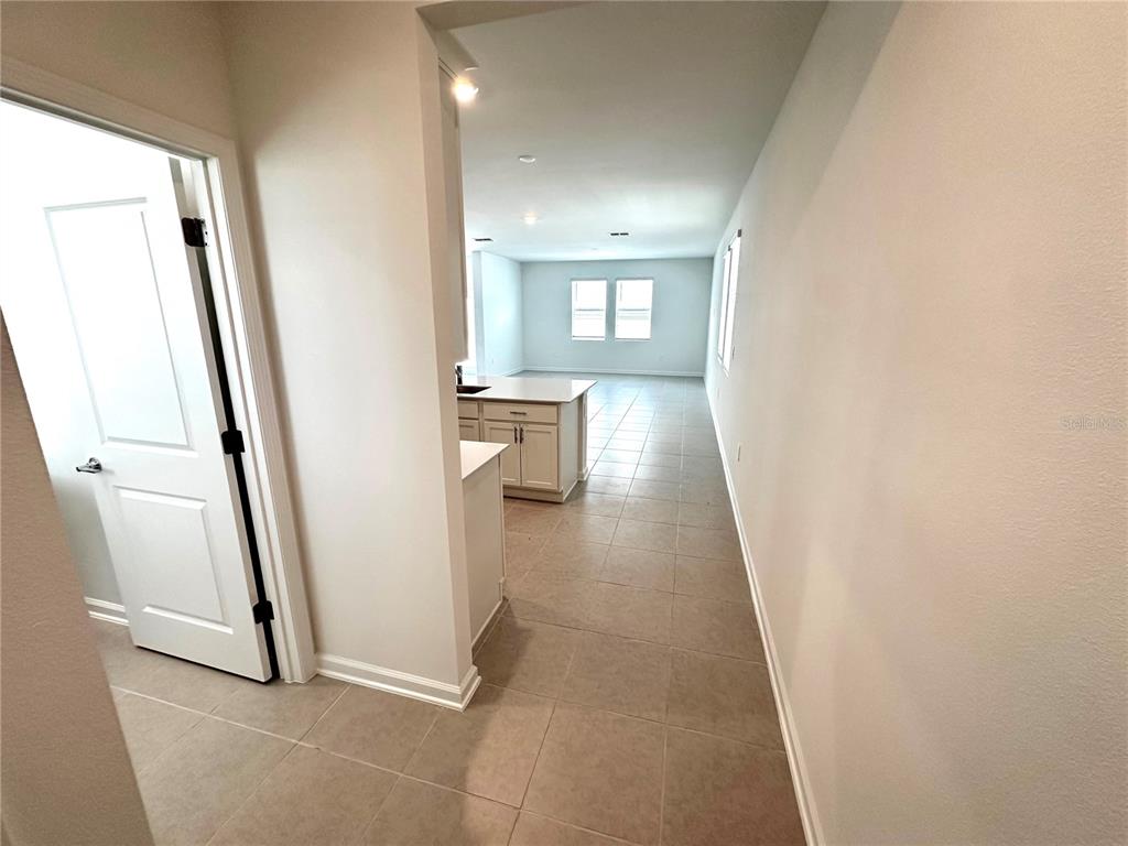 A view from a hallway looking into a kitchen and living area with tile flooring — 6095 WELLBEING WAY, CLERMONT, FL