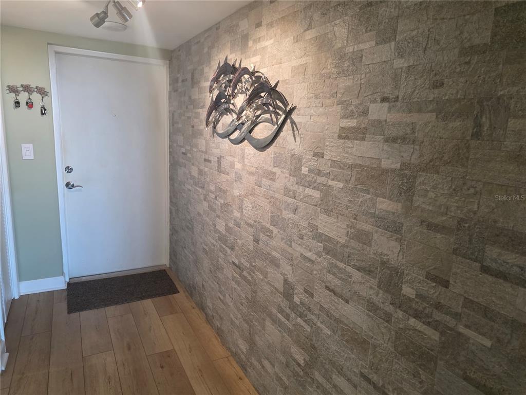 An entryway features a stone-tiled accent wall, wood-look flooring, and a metal wall sculpture — 5130 BRITTANY DRIVE S UNIT 604, ST PETERSBURG, FL