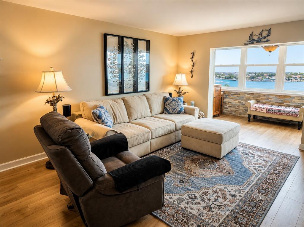 A living room features a beige sofa, a recliner, and a large window overlooking water — 5130 BRITTANY DRIVE S UNIT 604, ST PETERSBURG, FL