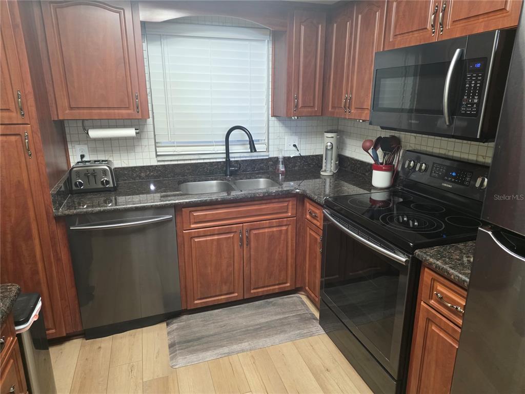 A kitchen with wood cabinets, dark granite countertops, stainless steel appliances, and light wood flooring — 5130 BRITTANY DRIVE S UNIT 604, ST PETERSBURG, FL