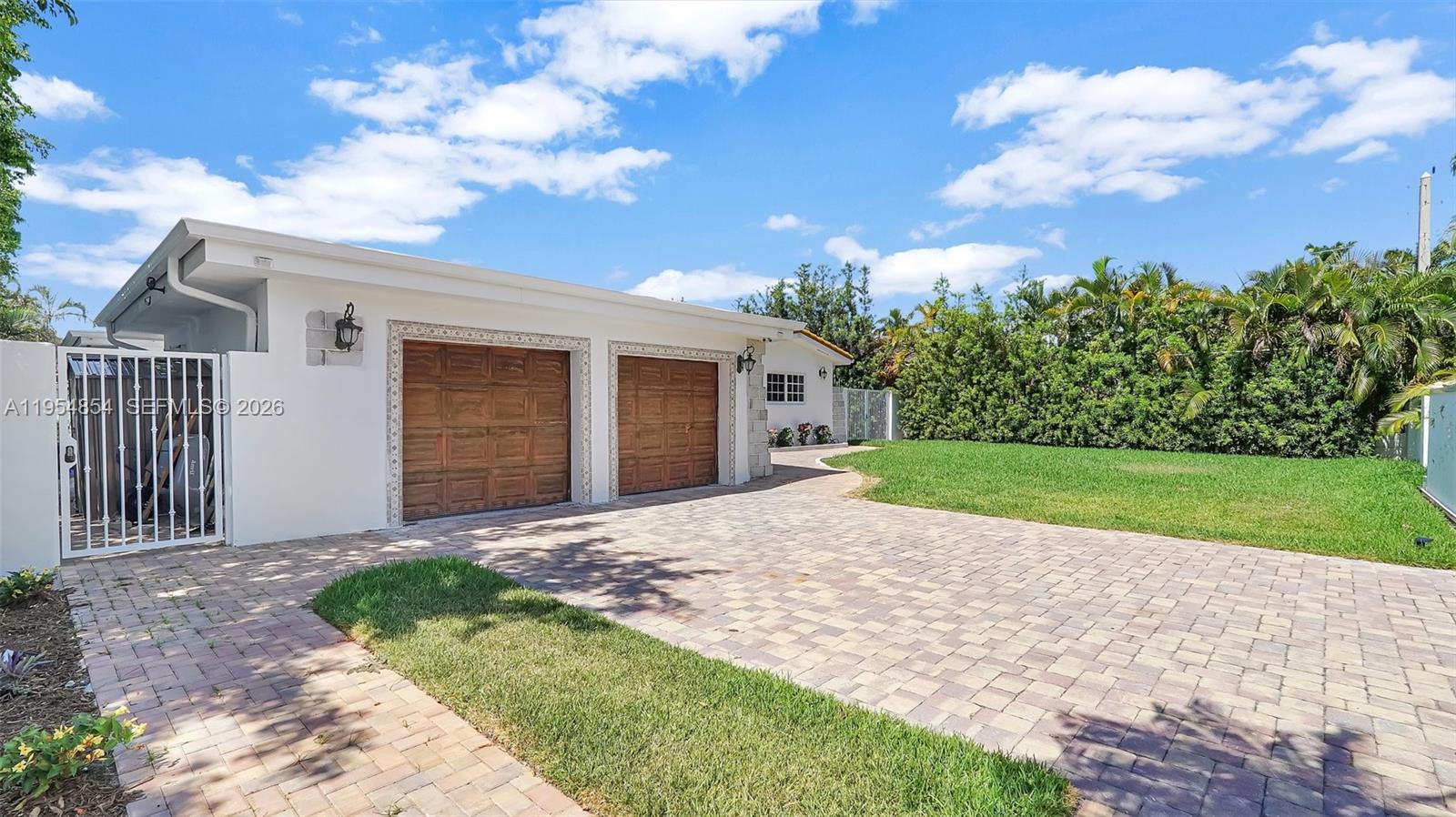 A white house features a two-car garage with wooden doors and a paved driveway — 1311 Pierce St, Hollywood FL 33019, HOLLYWOOD, FL
