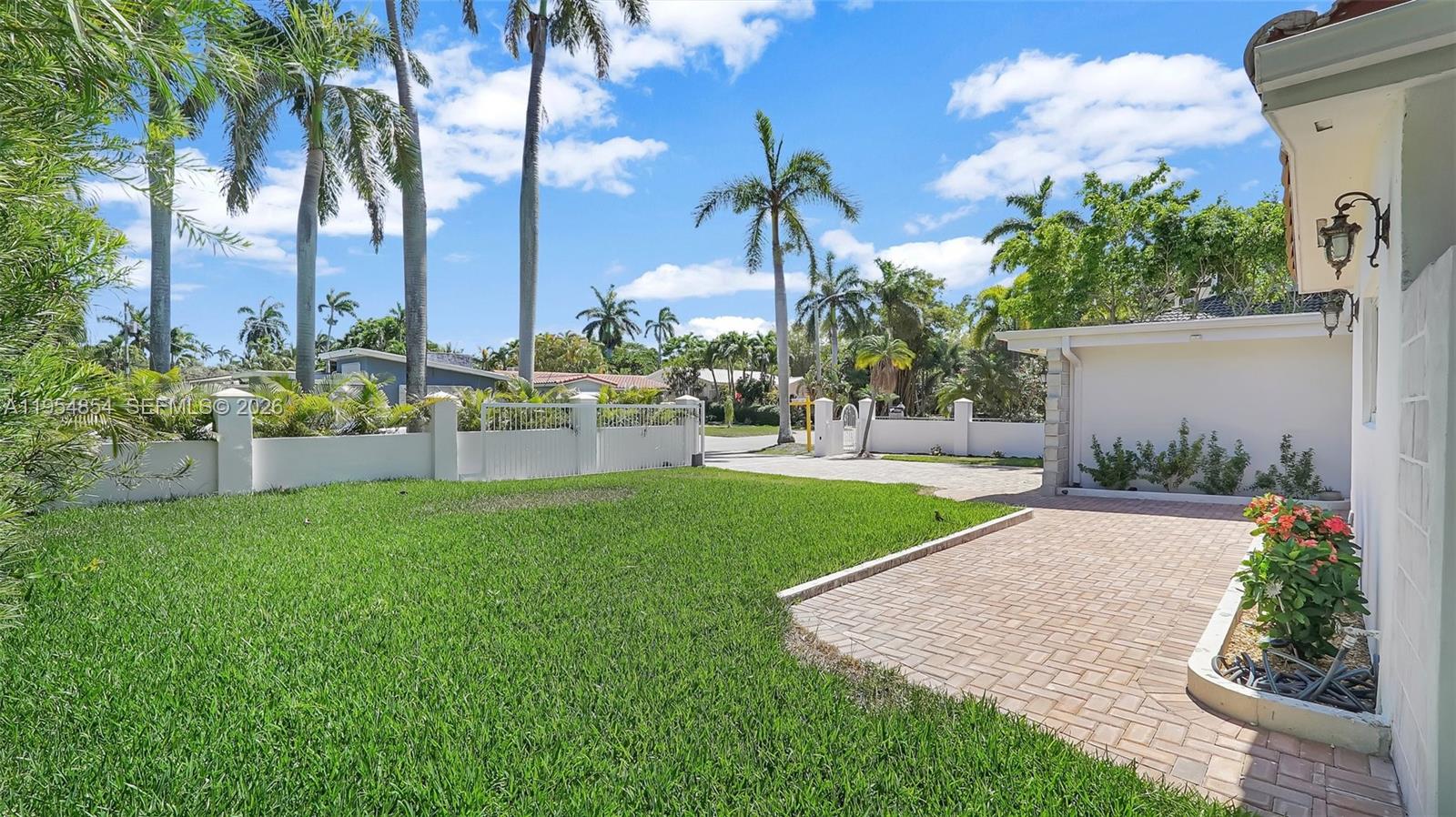A grassy front yard features a brick-paved driveway and a white perimeter wall — 1311 Pierce St, Hollywood FL 33019, HOLLYWOOD, FL