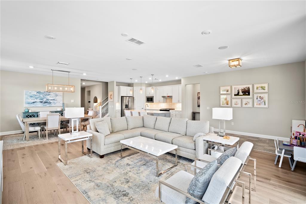 An open-concept living and dining area features light wood flooring, a sectional sofa, and kitchen — 12537 AQUA RESERVE COURT, FORT MYERS, FL