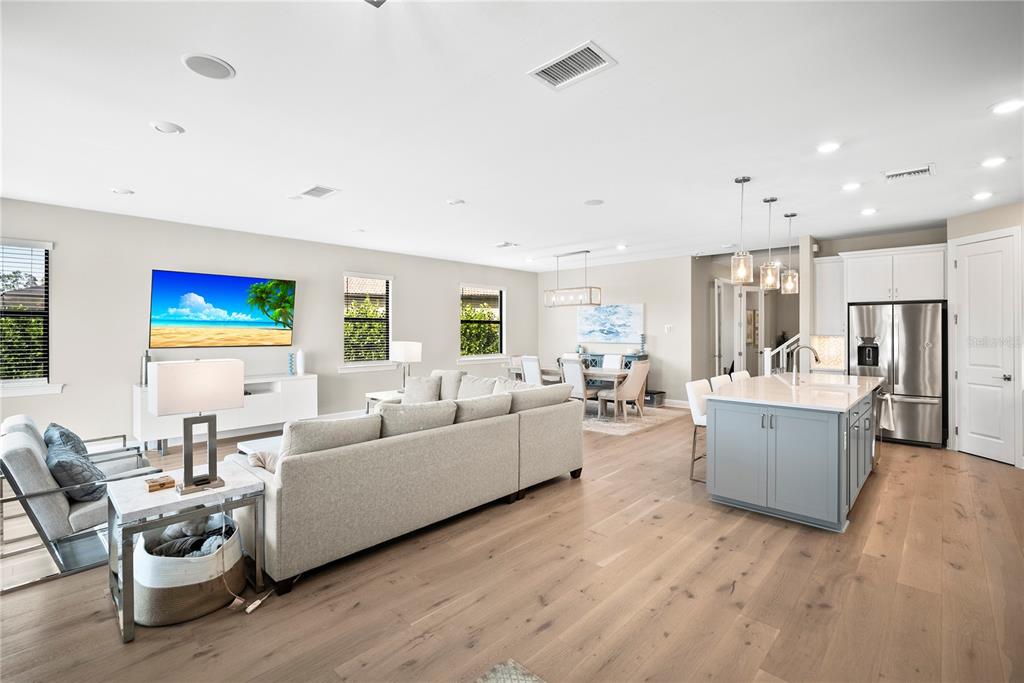 An open-concept living room and kitchen feature light wood floors, a sectional sofa, and island — 12537 AQUA RESERVE COURT, FORT MYERS, FL
