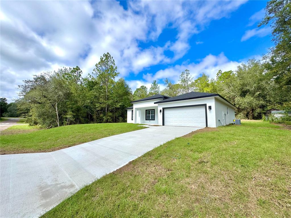A modern white house with a black roof and garage sits on a grassy lot — 9210 N HUNTER WAY, CITRUS SPRINGS, FL