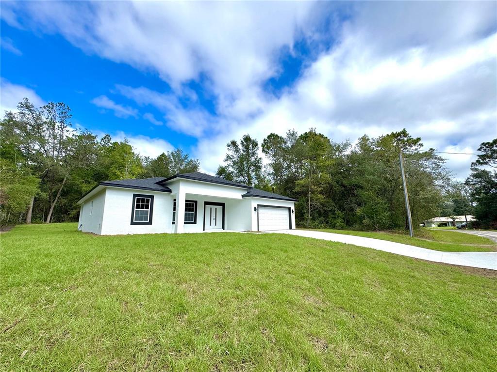 A white single-story house with a black roof and garage sits on a grassy lot — 9210 N HUNTER WAY, CITRUS SPRINGS, FL